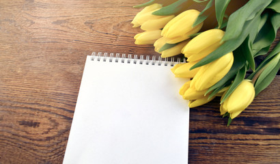 Yellow tulips bouquet with empty blank notepad  on wooden background. Greeting mock up concept for Mothers day, Womens day, Easter or wedding. Sunlight effect