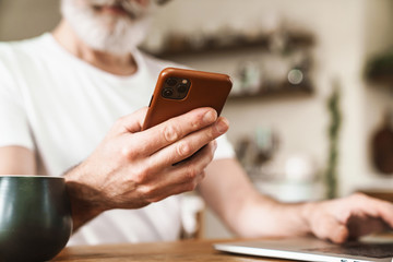 Cropped image of mature man working with laptop and smartphone