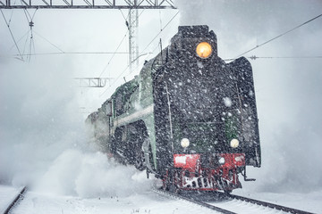 Retro steam train departs from the railway station at winter snowy time.