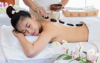 Obraz na płótnie Canvas Asian woman receive hot stone massage and treatment by a professional masseuse in spa salon. Healthy massage for relieve back pain
