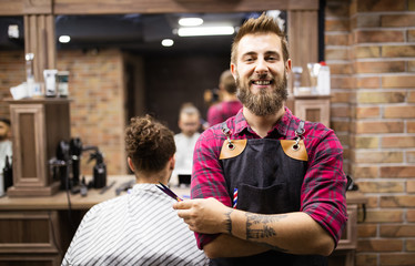 Portrait of happy young barber with client at barbershop and smiling.