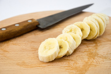 banana slices and knife on a wooden board on a white background. Close-up.