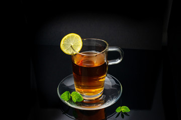 glass cup of tea, lemon and mint on a black background close-up