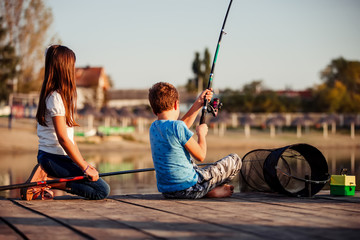 Two young cute little friends fishing on a lake in a sunny summer day