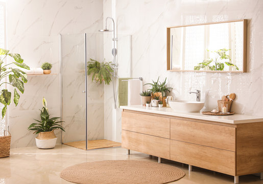 Stylish bathroom interior with countertop, shower stall and houseplants. Design idea