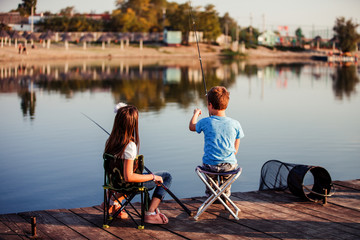 Two young cute little friends, boy and girl fishing on a lake in a sunny summer day