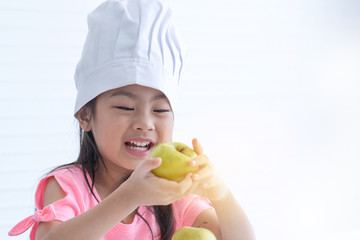 Happy little girl with chef hat holding green apple in hand over white background, kid chef