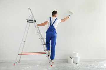 Man painting wall with white dye indoors, back view