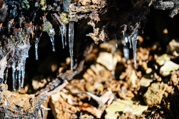 Icy little stalactite outdoors in nature on an overhang near stones.