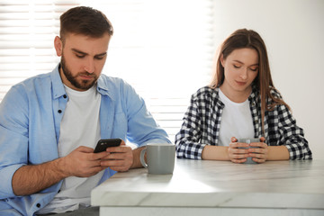 Fototapeta premium Young man preferring smartphone over his girlfriend at home. Relationship problems