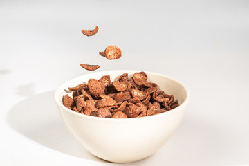 Chocolate corn flakes falling to the white bowl isolated on white. Motion.