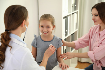 Fototapeta premium Mother and daughter visiting pediatrician. Doctor examining little patient with stethoscope in hospital
