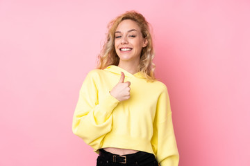 Young blonde woman wearing a sweatshirt isolated on pink background giving a thumbs up gesture