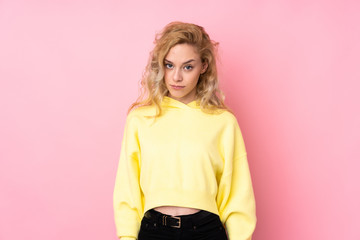 Young blonde woman wearing a sweatshirt isolated on pink background with sad and depressed...