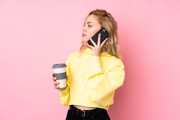 Obraz premium Young blonde woman wearing a sweatshirt isolated on pink background holding coffee to take away and a mobile