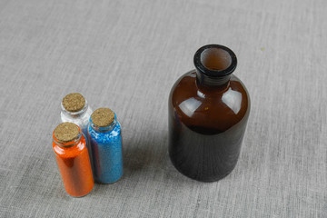 Blue, red and white powder and crystalls crystals in small bottles on gray linen background