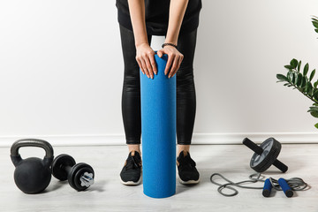 cropped view of sportswoman standing with fitness mat at home with sport equipment