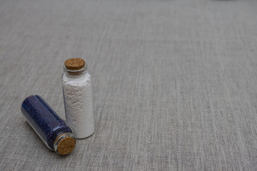 White and indigo powder and crystalls crystals in small bottles on gray linen background