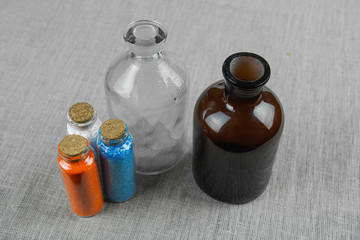 Blue, red and white powder and crystalls crystals in small bottles on gray linen background