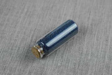 Blue powder and crystalls crystals in small bottle on gray linen background