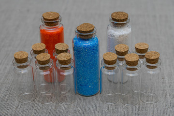 Blue, red and white powder and crystalls crystals in small bottles on gray linen background