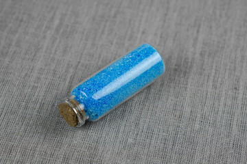 Blue powder and crystalls crystals in small bottle on gray linen background