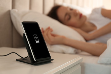 Smartphone charging on wireless pad and woman sleeping in bed