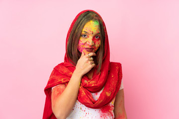 Young Indian woman with colorful holi powders on her face isolated on pink background thinking