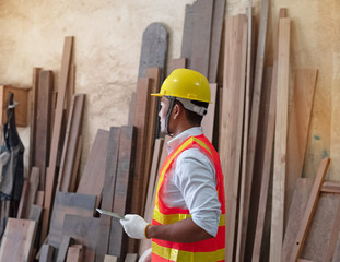 Handsome man wearing safety vest and yellow helmet,holding tablet in hand,for checking wood work at factory,blurry light around