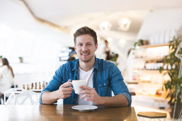 young handsome smiling man drinks coffee during his lunch break in the cafe, positive vibes