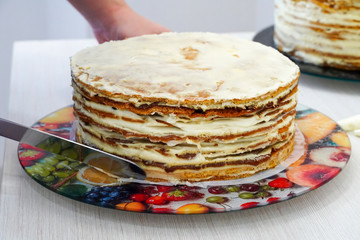 Cooking and leveling festive multilayer birthday cakes. Scones are smeared with whipped cream. Cook - Confectioner.