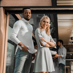 cheerful multicultural businesspeople looking at camera while multicultural colleagues standing on background