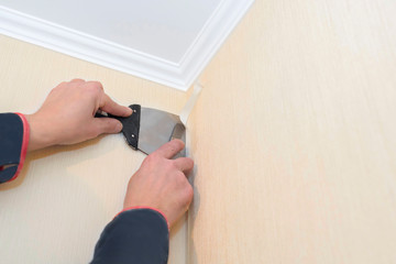 The builder cuts the wallpaper with a spatula and an office knife. Home repair concept. Details...