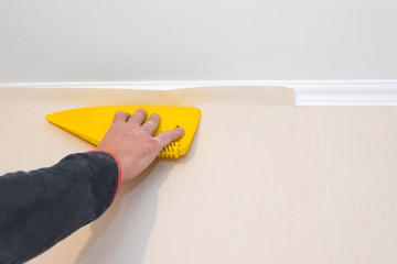 Hand smoothes the wallpaper with a plastic spatula on the wall during repair. Repair concept.