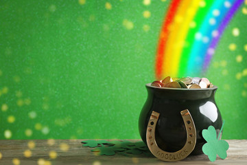 Pot with gold coins, horseshoe and clover leaves on wooden table against green background, space...