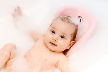 a small Caucasian baby is lying on a slide for bathing in foam