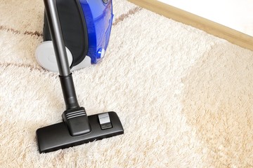Canister modern vacuum cleaner blue for cleaning the house on the background of a soft beige...