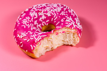 Bitten donut with glazed top isolated on a pink background
