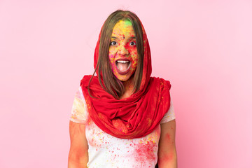 Young Indian woman with colorful holi powders on her face isolated on pink background with surprise facial expression