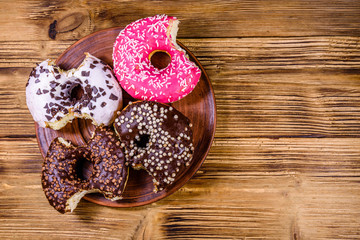Plate with bitten glazed donuts on a wooden table. Top view