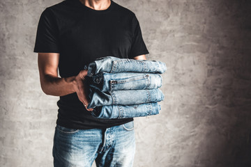 close up stack of folded denim blue jeans in hand over gray wall background, copy space