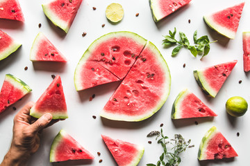 Red slices of ripe watermelon with mint leaves and lime slices on a white background. Top view