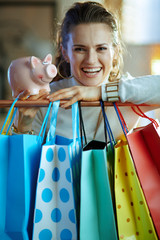 smiling modern woman near shopping bags showing piggy bank