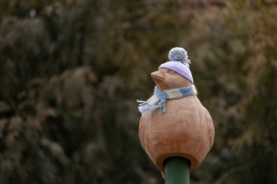 Decoration bird with hat and scarf sitting on a field. Bird with baked clay.