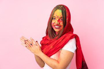 Young Indian woman with colorful holi powders on her face isolated on pink background scheming...