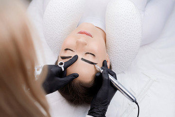 Beautiful young girl with long eyelashes tweezing her eyebrows in a beauty salon. Woman doing...
