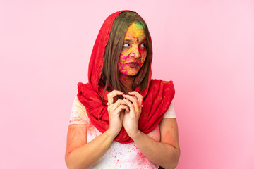 Young Indian woman with colorful holi powders on her face isolated on pink background scheming...