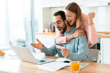 Portrait of young excited couple hugging while working with laptop