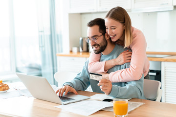 Portrait of young joyful couple hugging while working with laptop