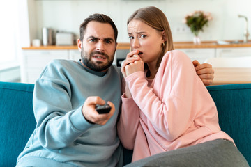 Portrait of young scared couple hugging and watching TV